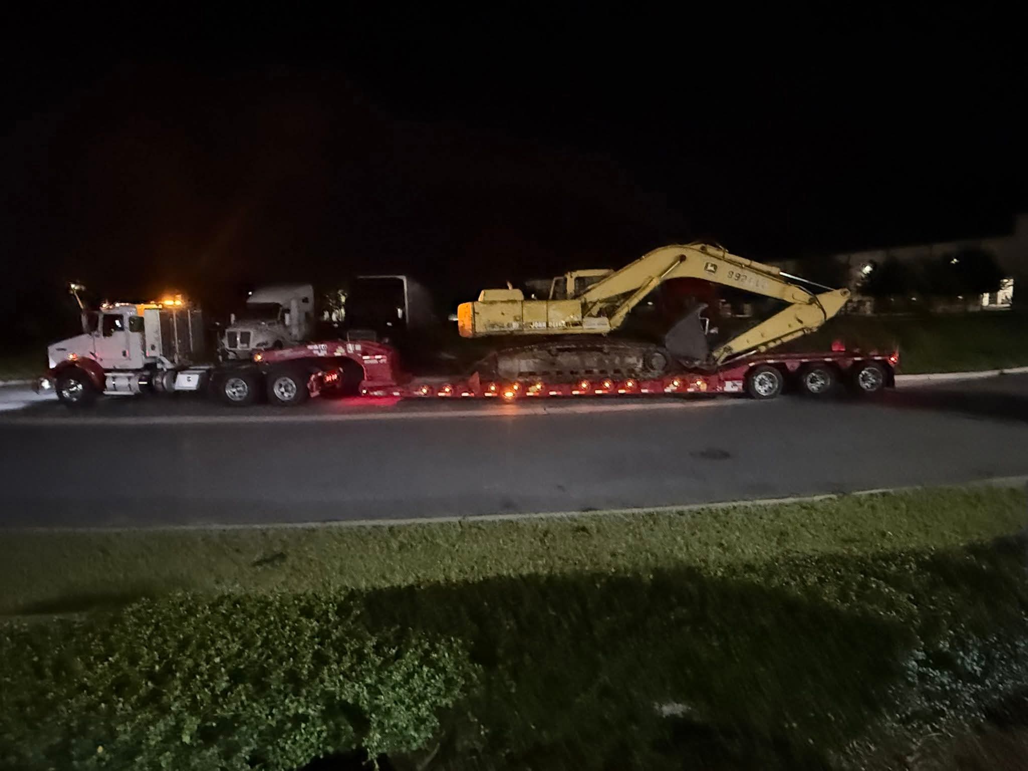 A truck transporting a large excavator on a flatbed trailer at night.